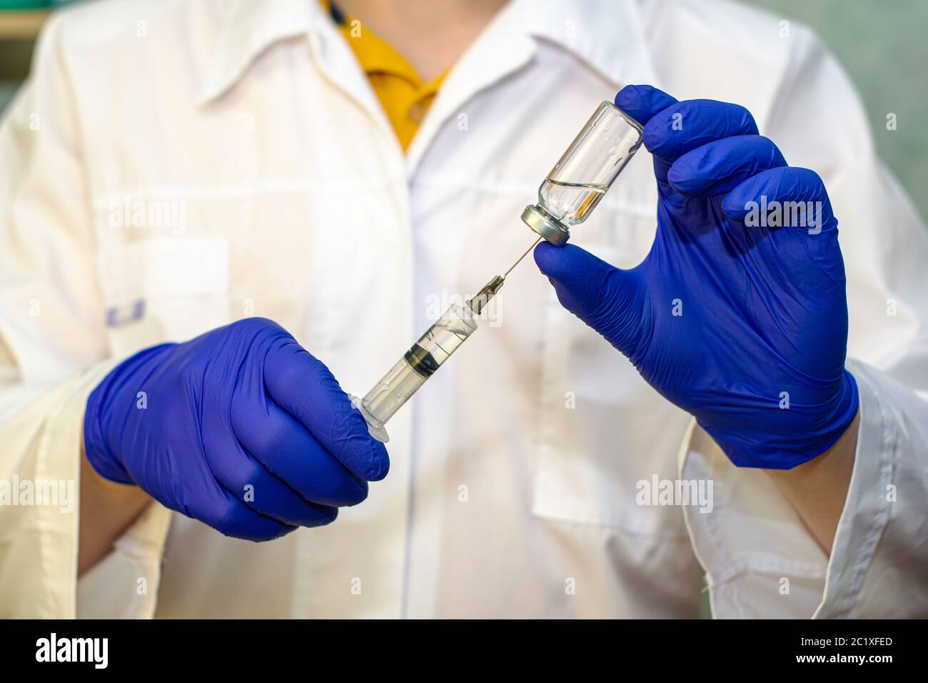 mains dans les gants chirurgicaux médicaux bleus, prélever le vaccin de l'ampoule avec une seringue. médecin dans le fond en flou Banque D'Images