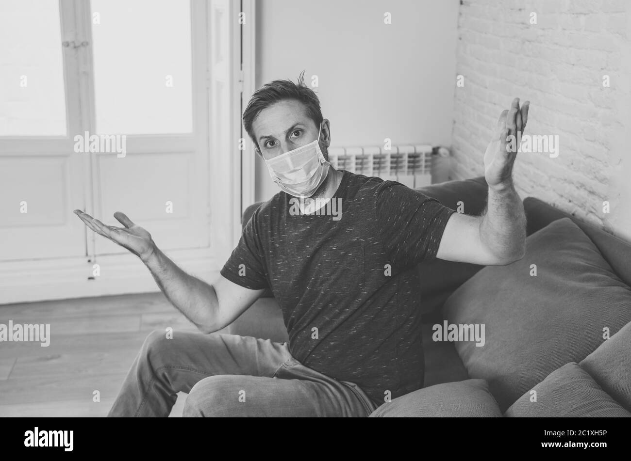 Triste homme avec masque protecteur à la maison salon canapé se sentant fatigué et inquiet souffrant de dépression dans le cadre du blocage du coronavirus et de la maladie sociale Banque D'Images