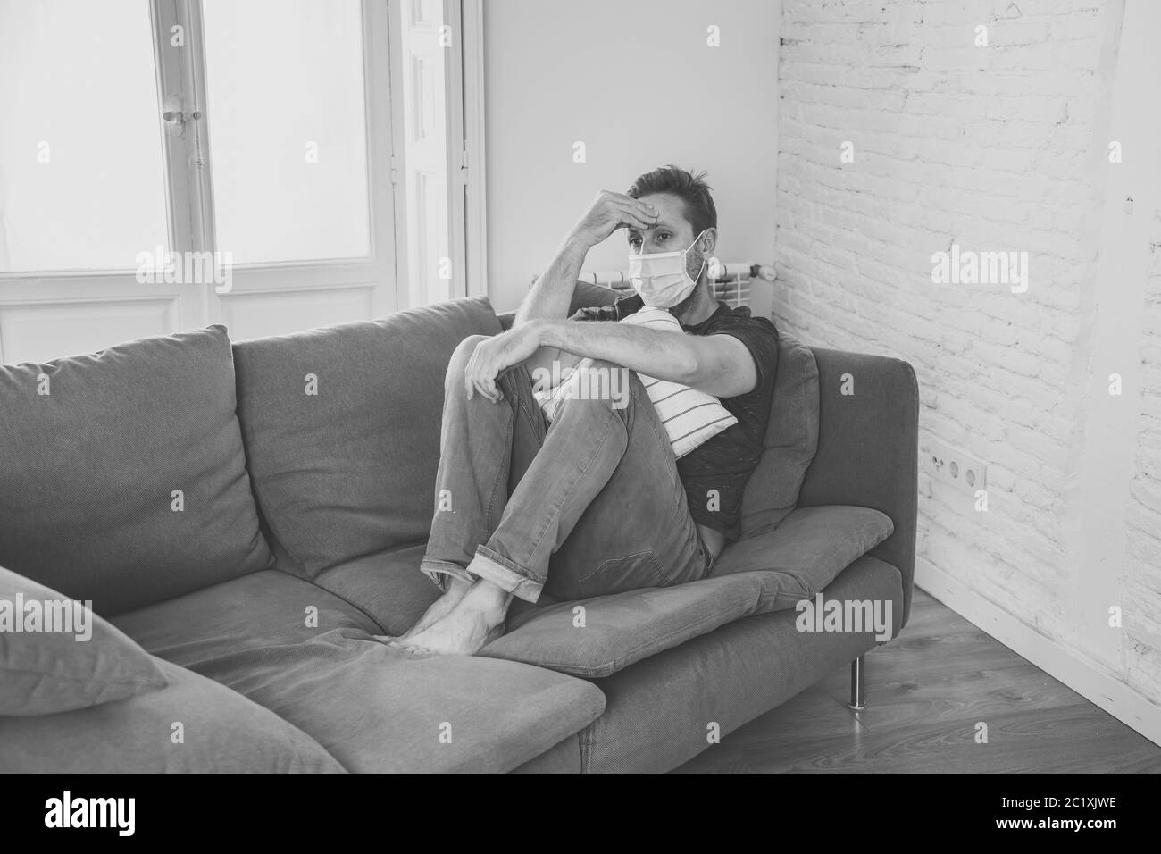 Triste homme avec masque protecteur à la maison salon canapé se sentant fatigué et inquiet souffrant de dépression dans le cadre du blocage du coronavirus et de la maladie sociale Banque D'Images