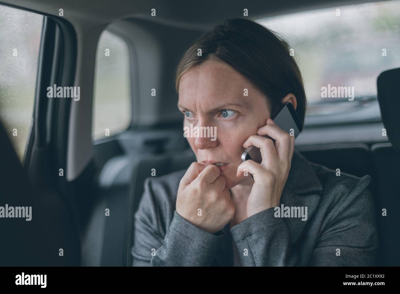 Femme d'ongles mordant nerveux et talking on mobile phone sur le siège arrière d'une voiture Banque D'Images