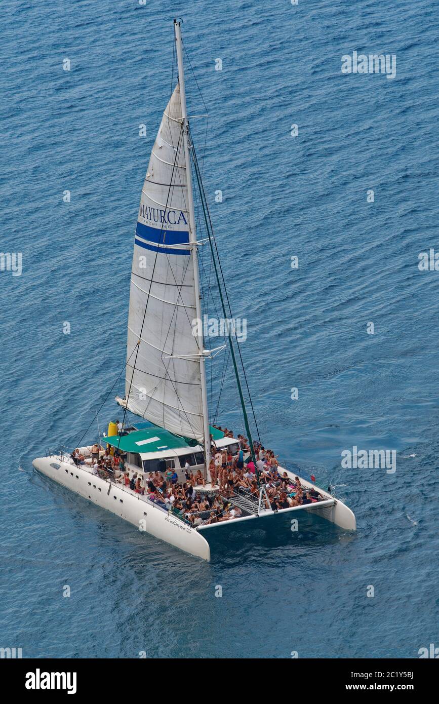 Catamaran plein de jeunes lors d'une excursion en bateau de fête le long de la côte de la péninsule de Llevant, près de Port d'Alcudia, côte nord-est de Majorque, août. Banque D'Images