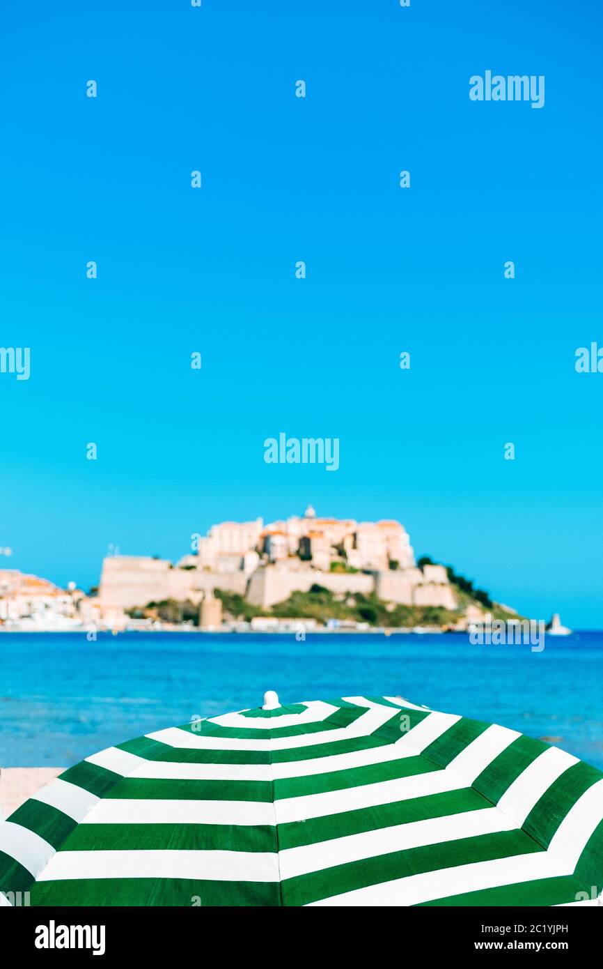 Vue sur Calvi, en Corse, France, avec sa célèbre citadelle sur le bakcground au sommet d'un promontoire, et un parasol et la mer Méditerranée Banque D'Images