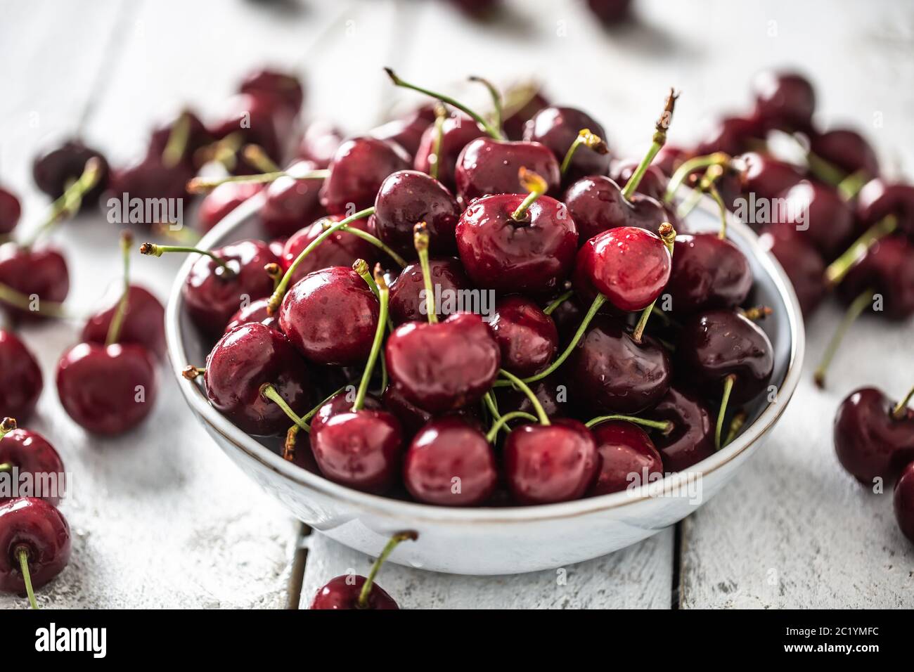 Cerises fraîches lavées à l'eau propre dans un bol et dispersées tout autour Banque D'Images