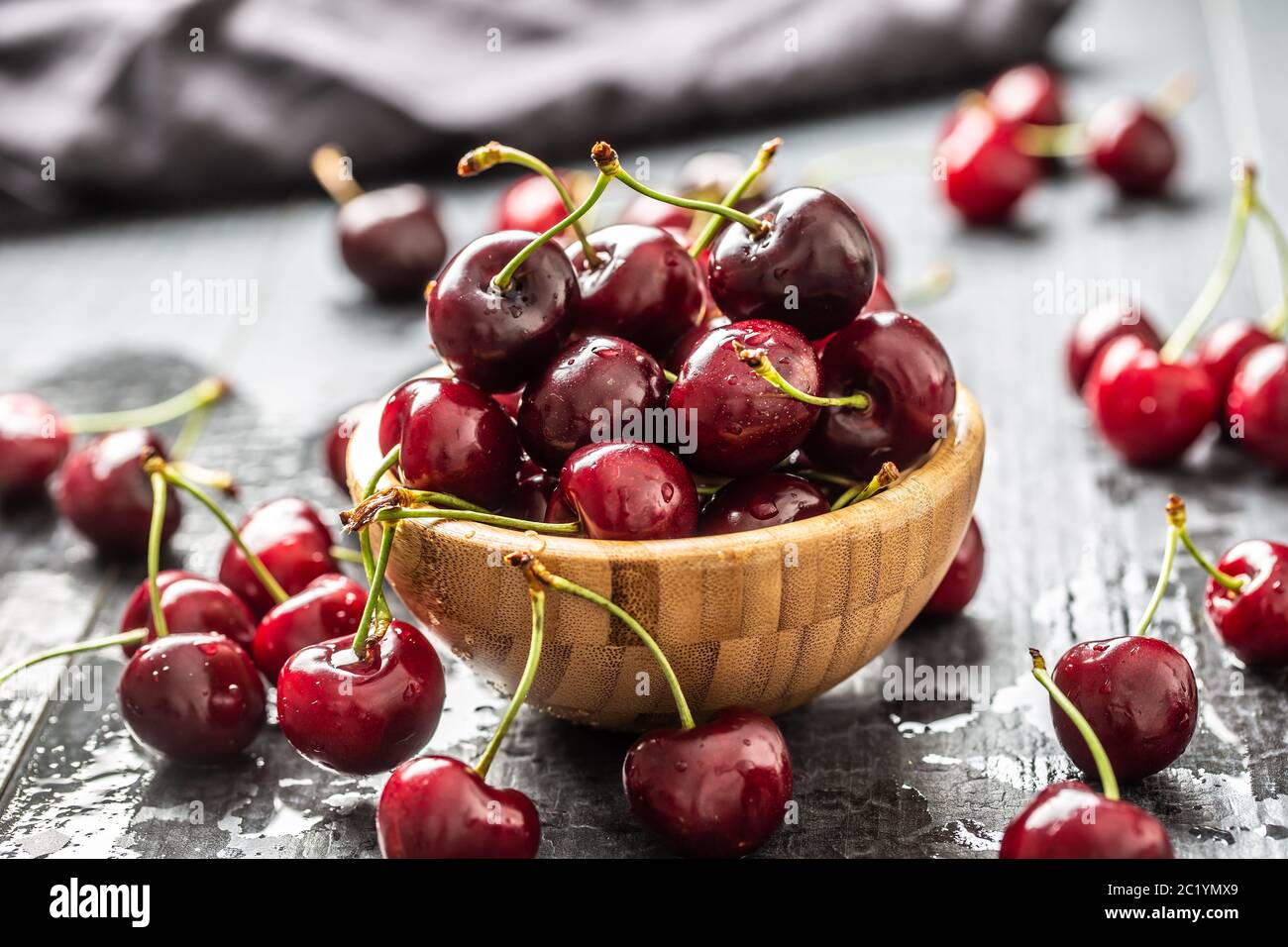 Cerises fraîches lavées à l'eau propre dans un bol et dispersées tout autour Banque D'Images