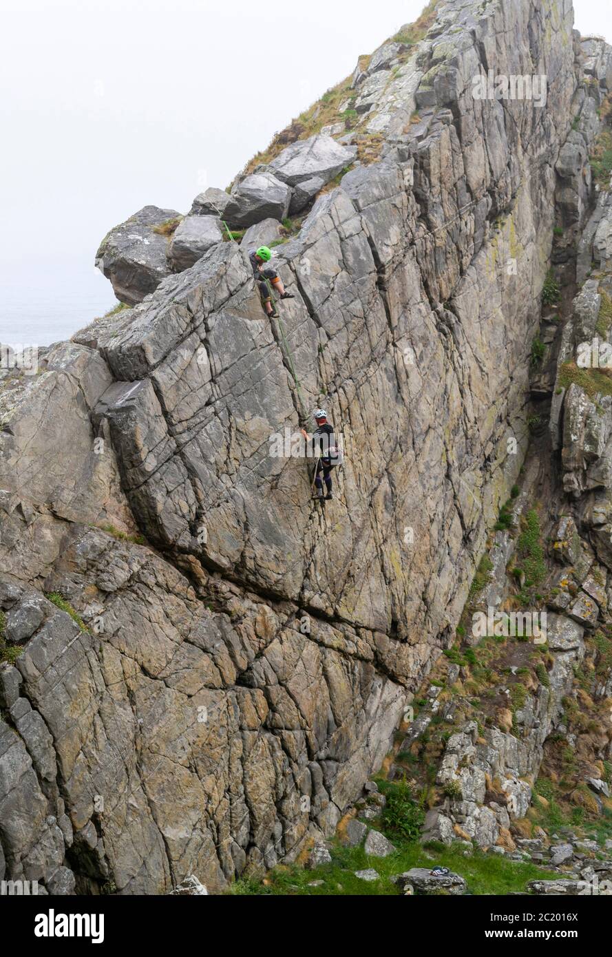 CULLEN VILLE MORAY CÔTE ÉCOSSE DEUX PERSONNES SUR UN VISAGE DE ROCHE UTILISÉ PAR LES GRIMPEURS DE ROCHE Banque D'Images