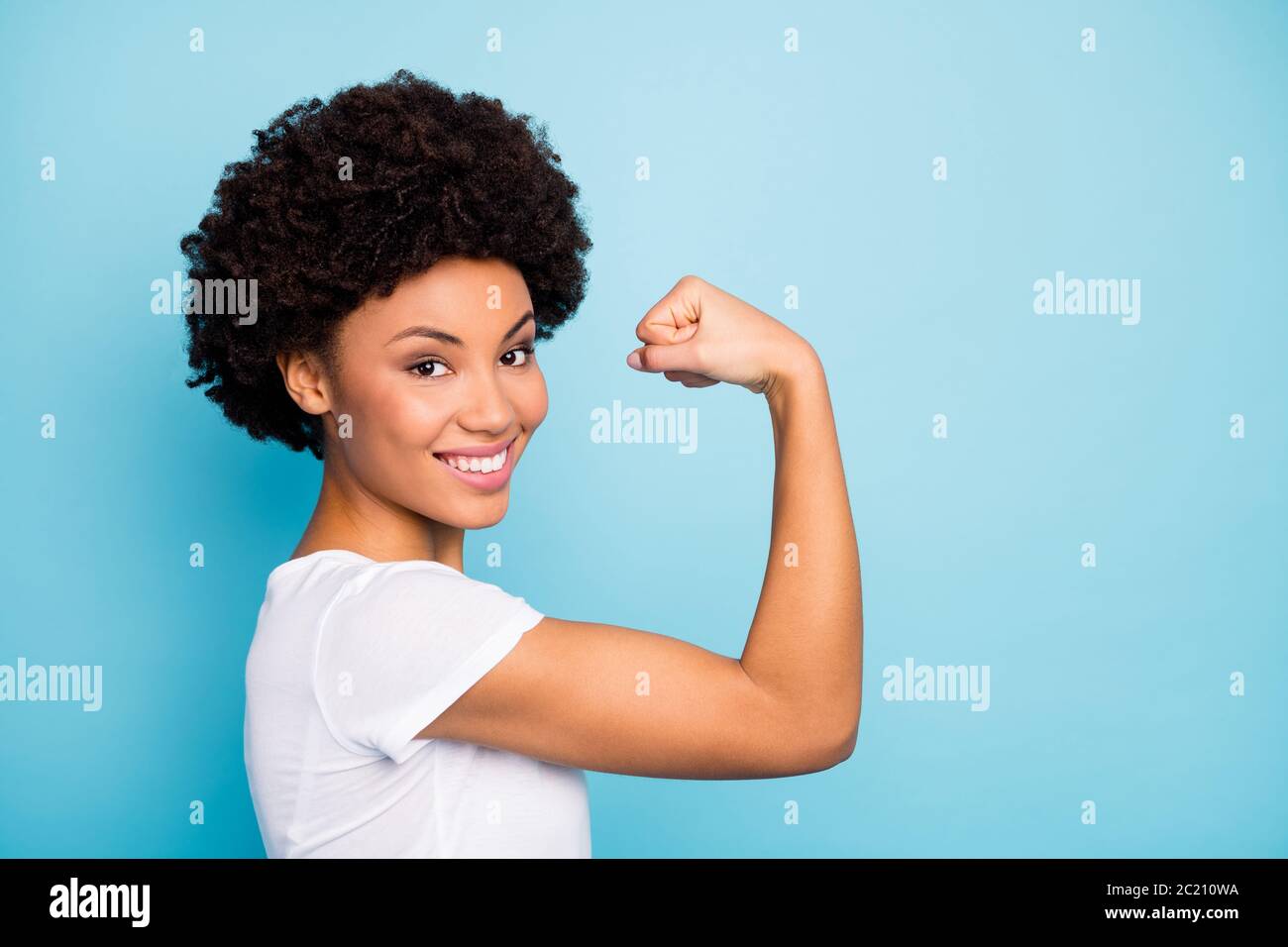 Gros plan photo de profil de belle peau sombre femme en forme de curly montrant la forme parfaite biceps après l'entraînement intense vêtements de gym décontracté blanc t-shirt isolé Banque D'Images