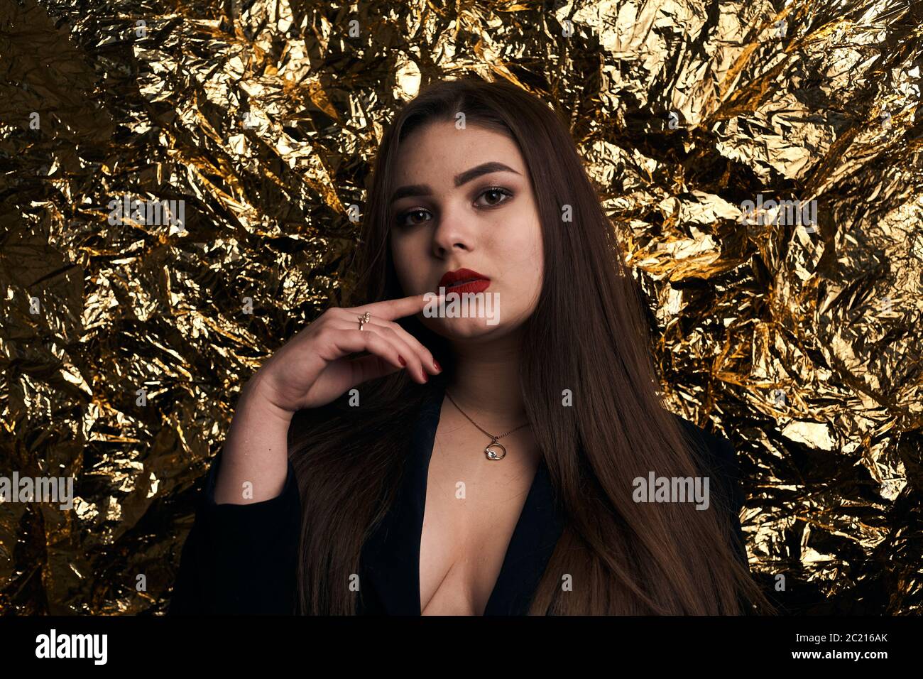 Une fille chic et doubée pose dans une veste noire sur fond doré. Banque D'Images