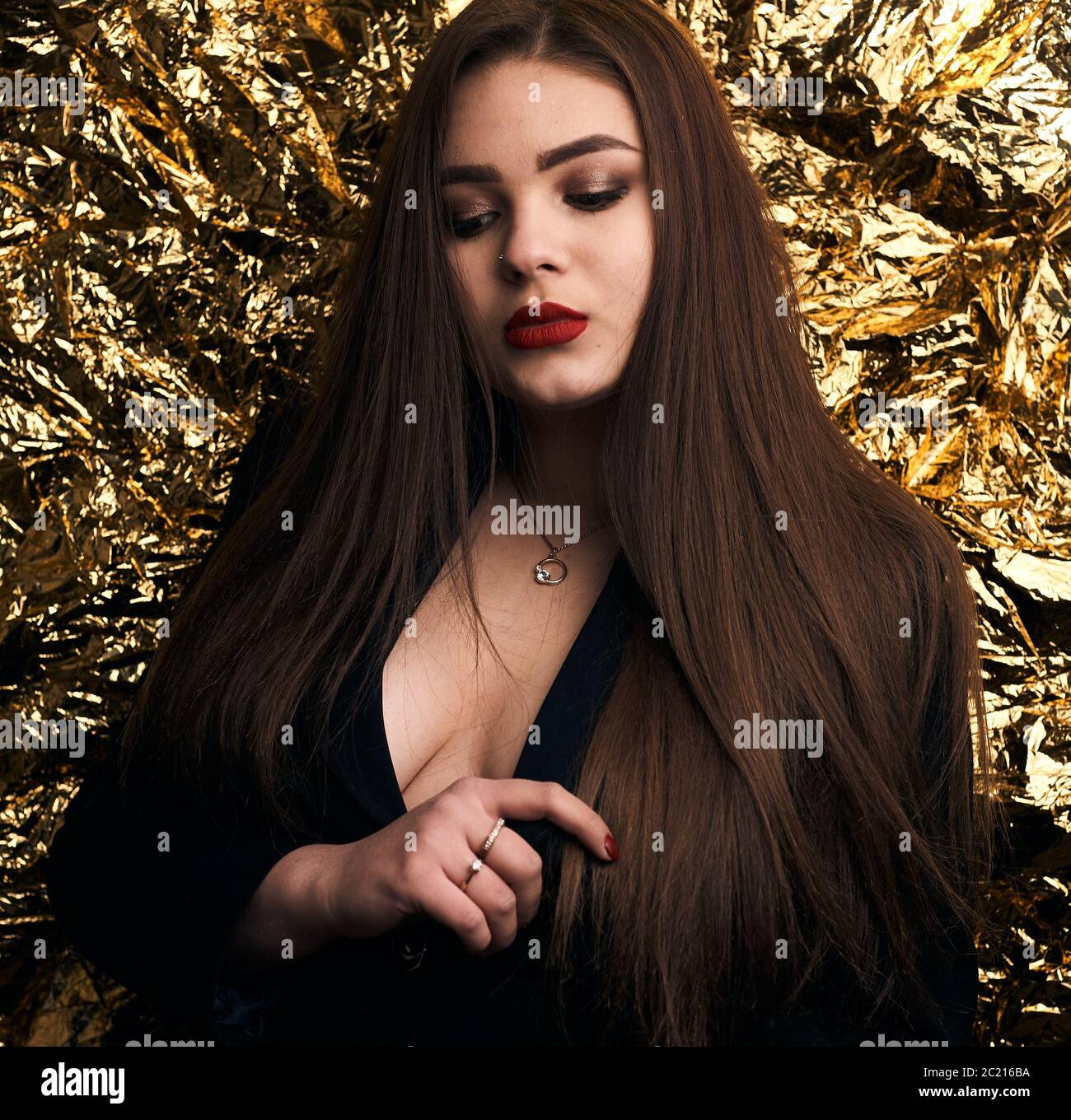 Une fille chic et doubée pose dans une veste noire sur fond doré. Banque D'Images