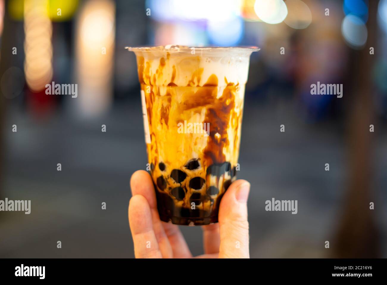 Main tenant une tasse en plastique de thé au lait de sucre noir ( thé de bulle ) avec fond de bokeh flou Banque D'Images
