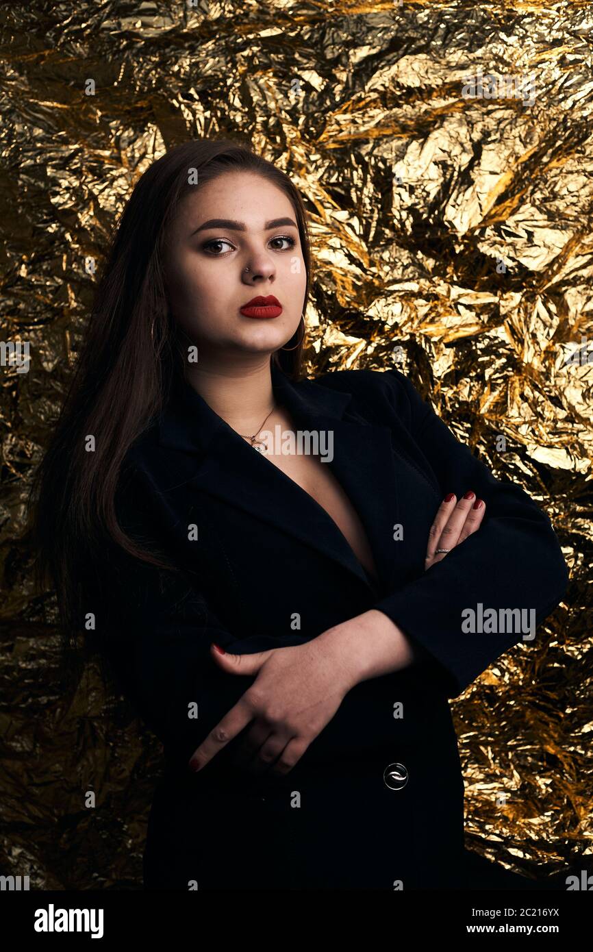 Une fille chic et doubée pose dans une veste noire sur fond doré. Banque D'Images