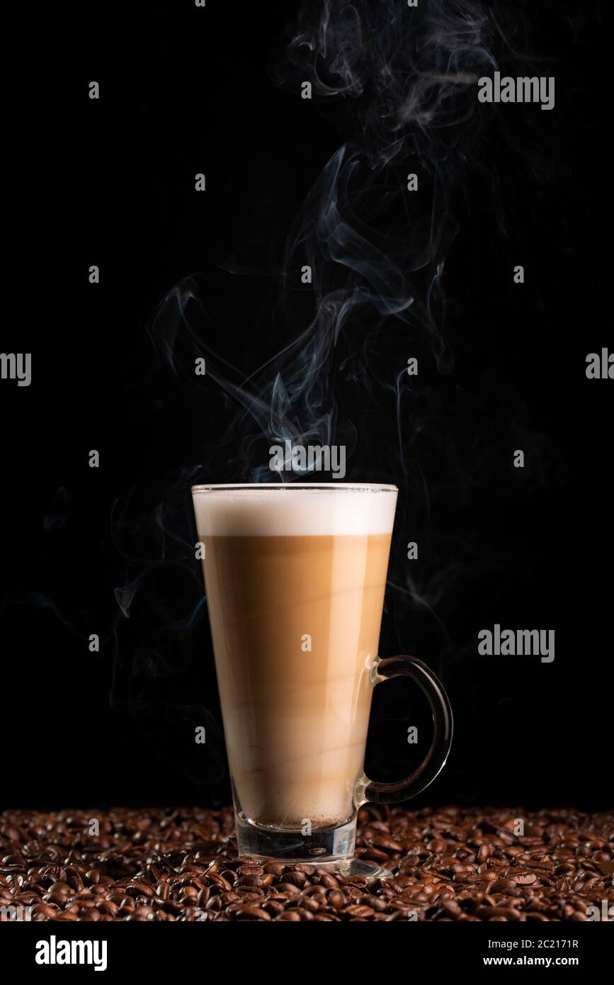 Latte de café à la vapeur avec mousse de lait dans un grand verre, sur des grains de café. Banque D'Images