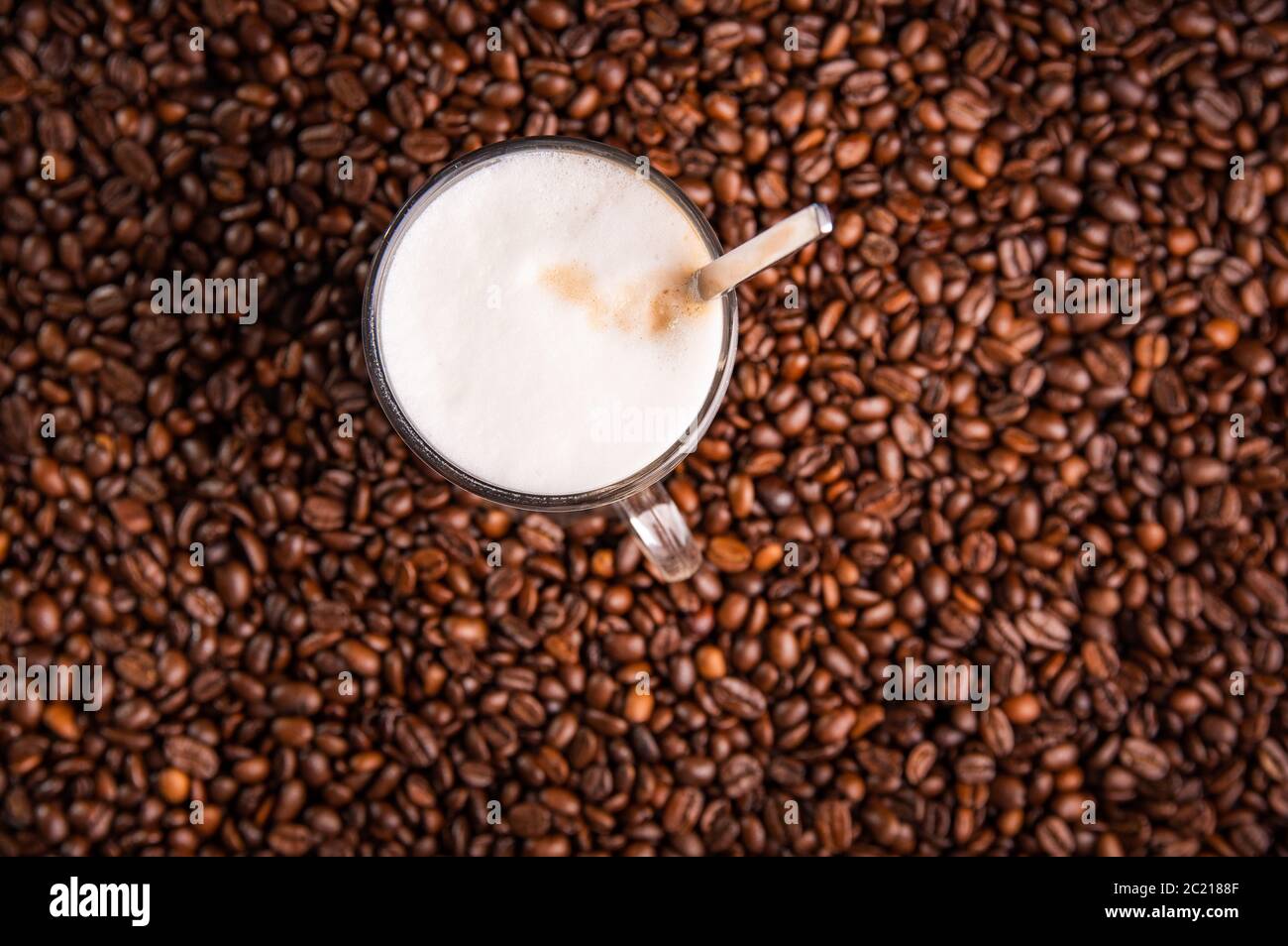 Latte à café avec mousse de lait dans un grand verre, sur des grains de café. Banque D'Images