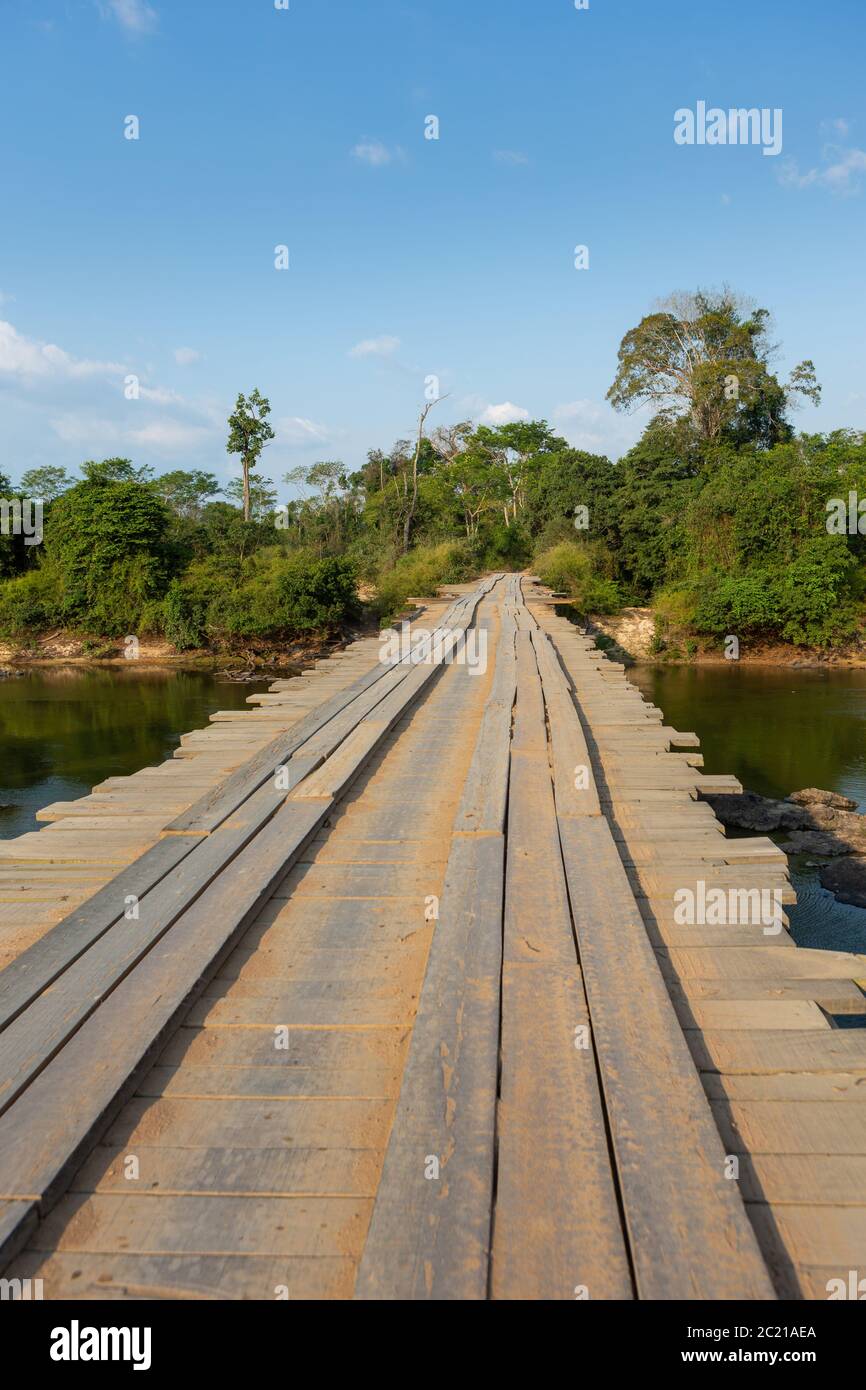 route dangereuse de terre traversant un pont rustique en bois sur la rivière dans la forêt amazonienne. Point de vue du conducteur. Concept de transport, logistique, voyage, aventure Banque D'Images