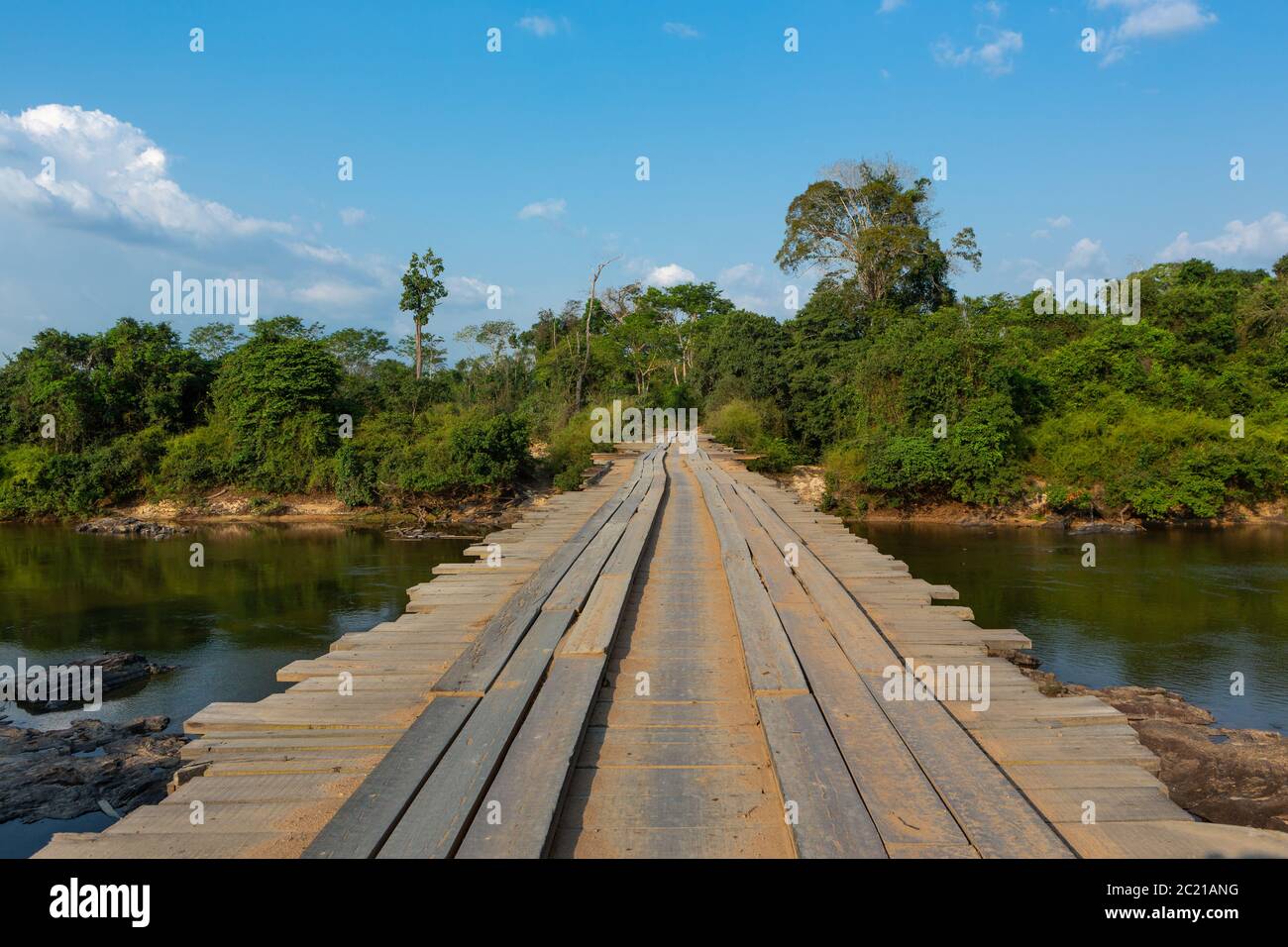 route dangereuse de terre traversant un pont rustique en bois sur la rivière dans la forêt amazonienne. Point de vue du conducteur. Concept de transport, logistique, voyage, aventure Banque D'Images