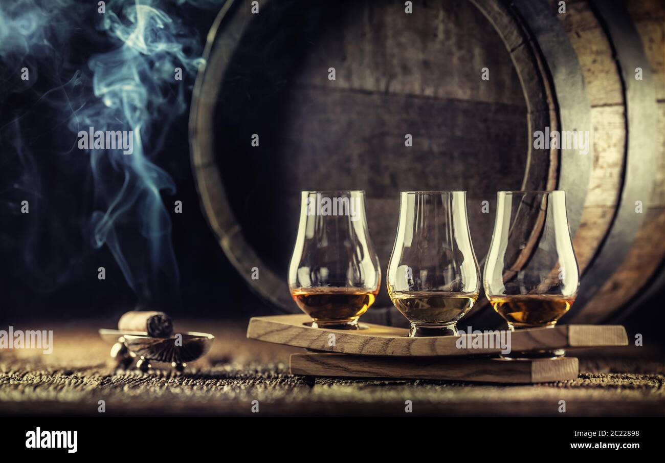 Dégustation de whisky Glencairn sur un service en bois, avec un fût de whisky dans le fond sombre et un cigare fumant à côté Banque D'Images