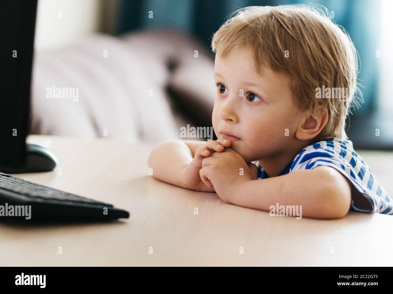 Un enfant, un garçon dans une veste jaune, est assis à une table à la maison regardant un ordinateur portable, l'apprentissage en ligne, l'apprentissage à distance à la maison via Internet Banque D'Images