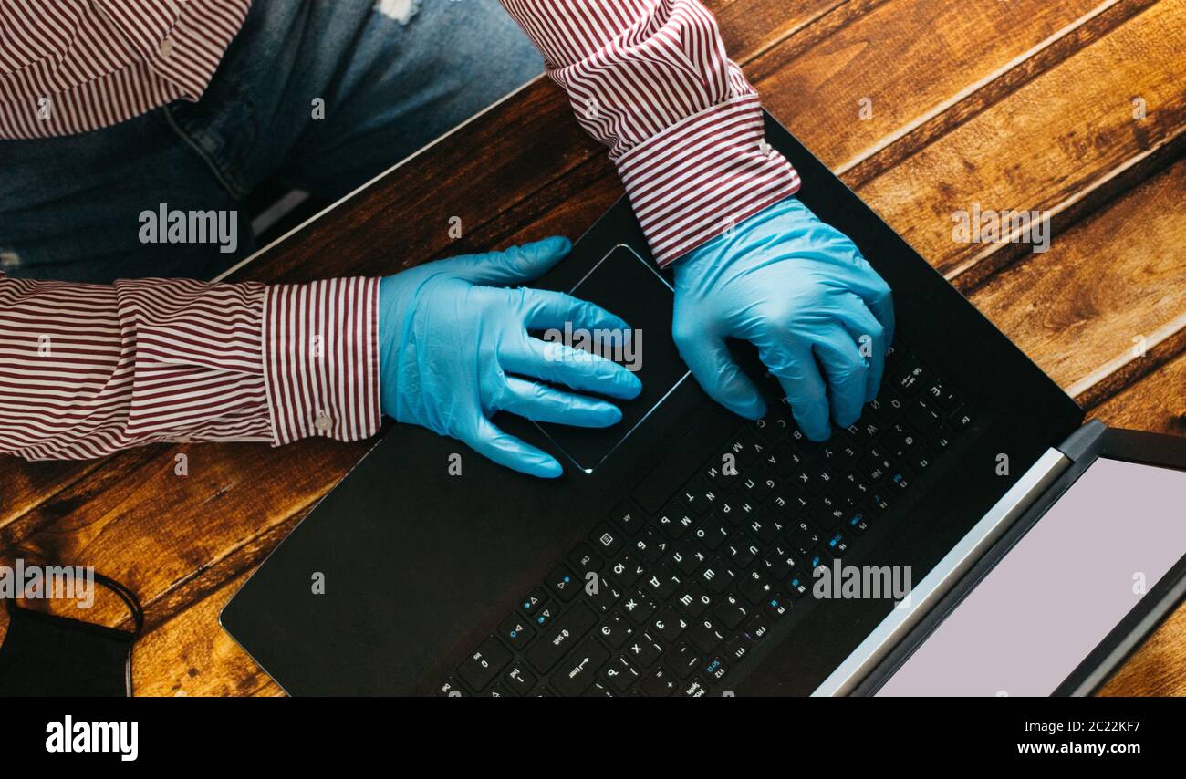 Un homme travaillant à domicile sur un ordinateur portable portant des gants jetables pour la protection. Épidémie de coronavirus. Homme d'affaires en quarantaine. Travail à domicile. Restez à Banque D'Images