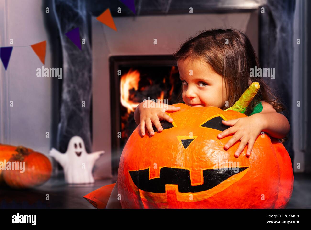 Petite fille se cache derrière la grande citrouille d'Halloween orange avec curieux look assis près de la cheminée Banque D'Images