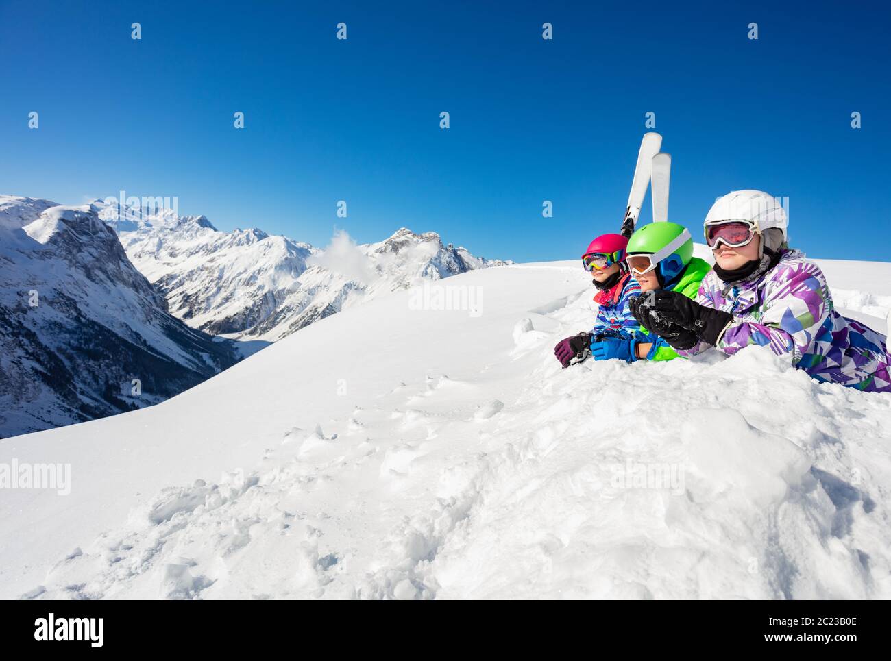 Groupe d'enfants heureux garçons et filles s'allonger dans la neige avec le ski dans une rangée regardant sur la chaîne de haute montagne Banque D'Images