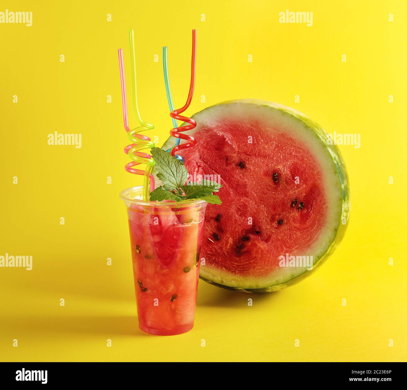 De smoothie pastèque rouge mûr dans une tasse en plastique, lot de tubes colorés et une feuille de menthe sur fond jaune Banque D'Images