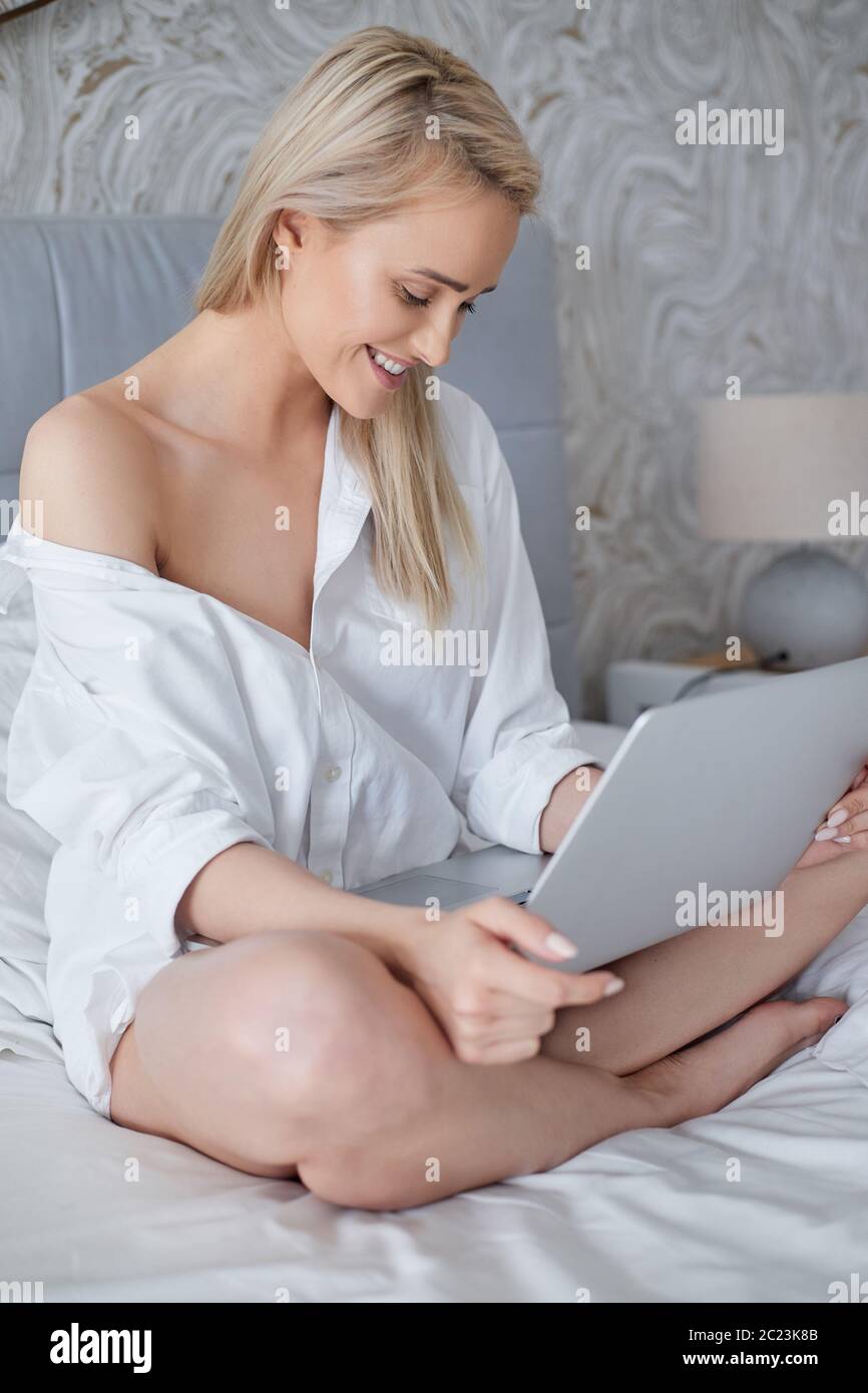 Femme Beatutiful dans une élégante chemise blanche pour homme assise dans  un lit avec ordinateur portable Photo Stock - Alamy