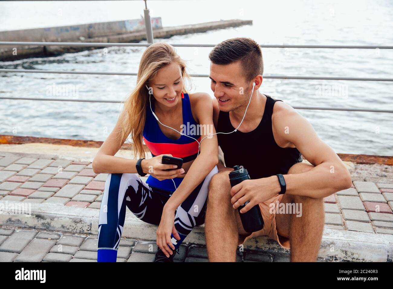 Belle Vue de face de la sportive et le sportif attrayant à regarder une vidéo amusante sur téléphone mobile, tout en restant assis sur le sol et se reposant après workou Banque D'Images