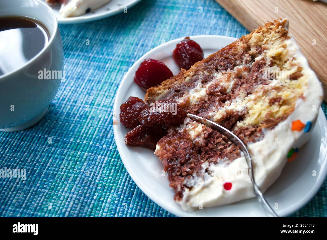 Un morceau de gâteau de Savoie au chocolat avec crème sur une assiette blanche, décoré de garnitures multicolores et de fraises confites Banque D'Images