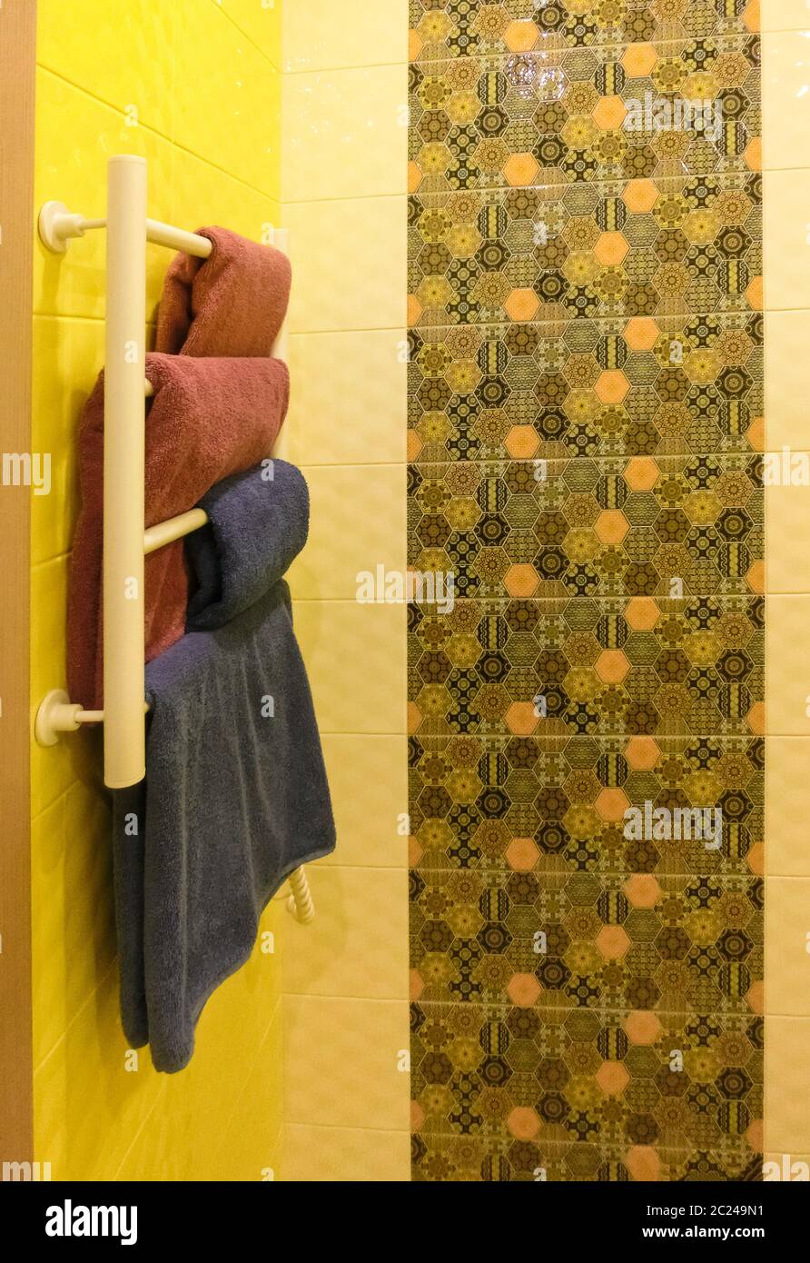 Salle de bains vide avec mur de douche gris derrière un porte-serviette en métal blanc avec des serviettes pliées sur le dessus Banque D'Images