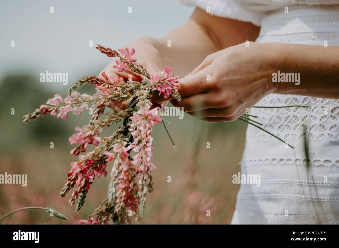 Gros plan sur les mains d'une femme qui tressent des fleurs sauvages dans une couronne de fleurs Banque D'Images