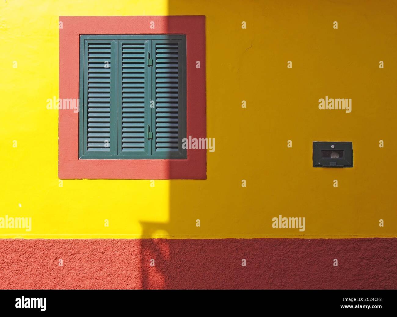 mur de maison coloré rouge et jaune vif avec un volet en bois vert dans un cadre carré en plein soleil et ombre Banque D'Images