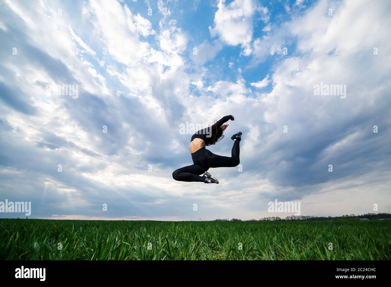 La jeune gymnaste professionnelle saute dans la nature contre le ciel bleu. Une athlète de fille dans un haut noir et des leggings noirs fait des exercices acrobatiques Banque D'Images