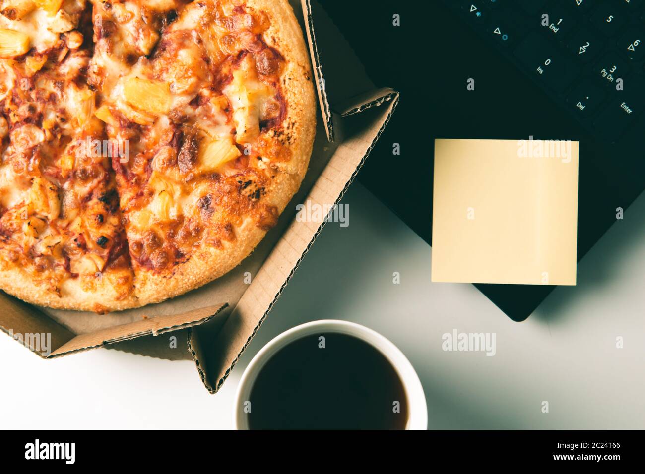 Pizza dans une boîte, tasse de café, ordinateur portable et étiquette vide avec espace pour les copies sur le bureau. Concept de livraison de nourriture ou de pizza et pause le jour ouvrable. Banque D'Images