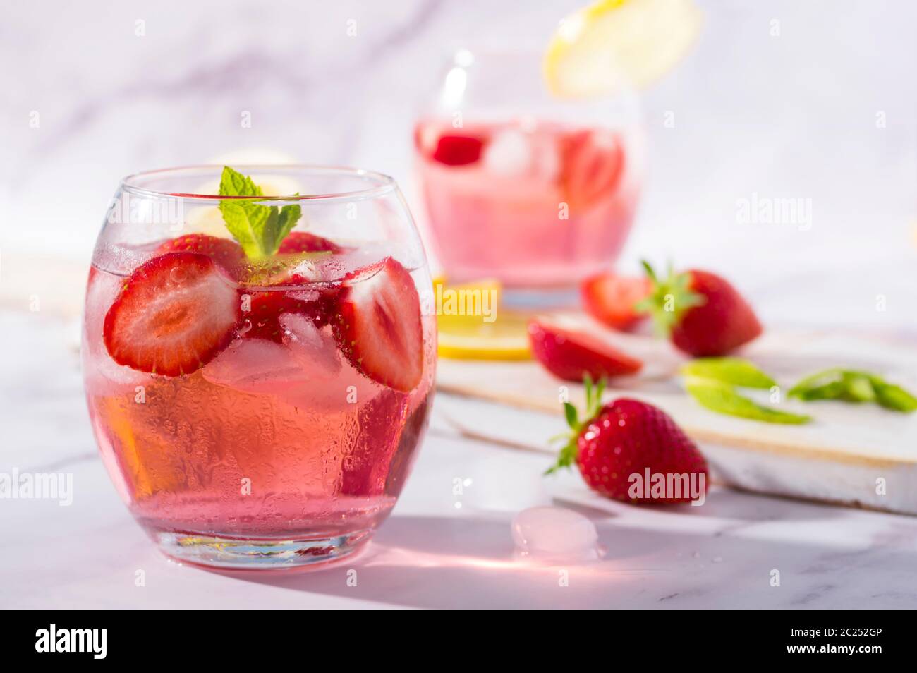 Gin et tonique aux fraises roses froides garni de fruits frais, de feuilles de citron et de menthe. Banque D'Images