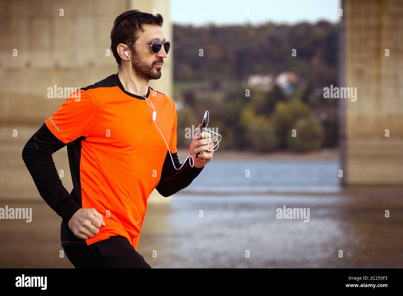 L'homme de la forme dans les vêtements de sport orange est le jogging en plein air avec des écouteurs et téléphone, concept de loisirs. Banque D'Images