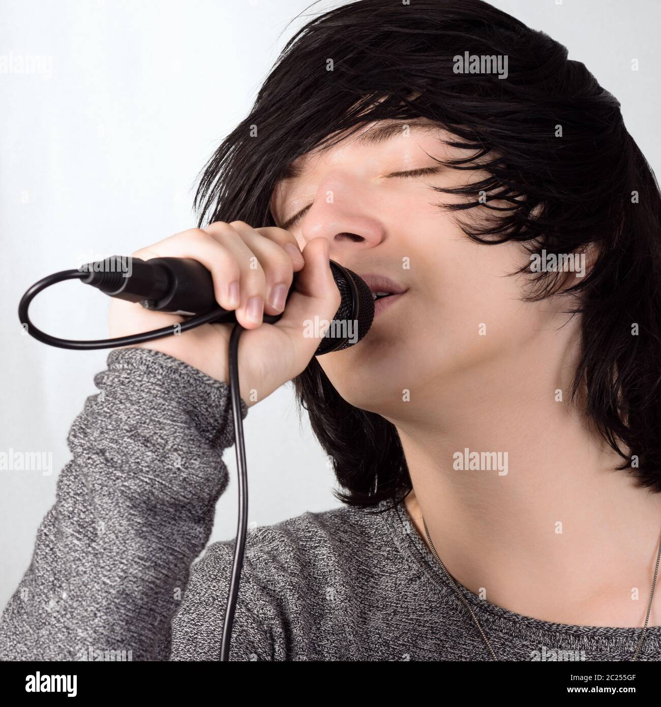 Cheveux noirs jeune gars en style emo chante dans le microphone sur fond blanc. Banque D'Images
