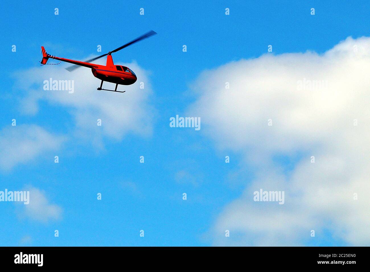 Un petit hélicoptère rouge vole à travers le ciel bleu avec des nuages blancs. Banque D'Images