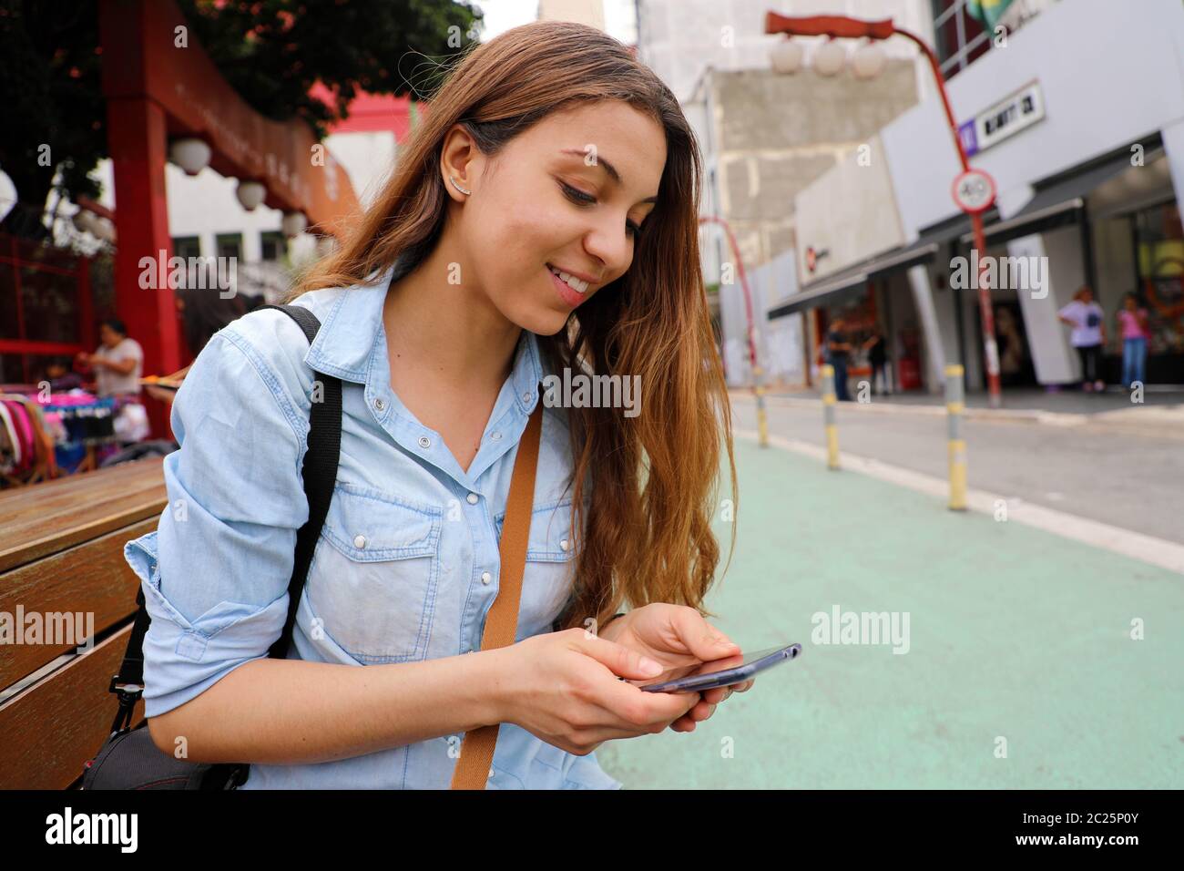 Belle étudiante fille assise sur le banc de la rue avec la messagerie téléphone mobile à Sao Paulo, Brésil Banque D'Images