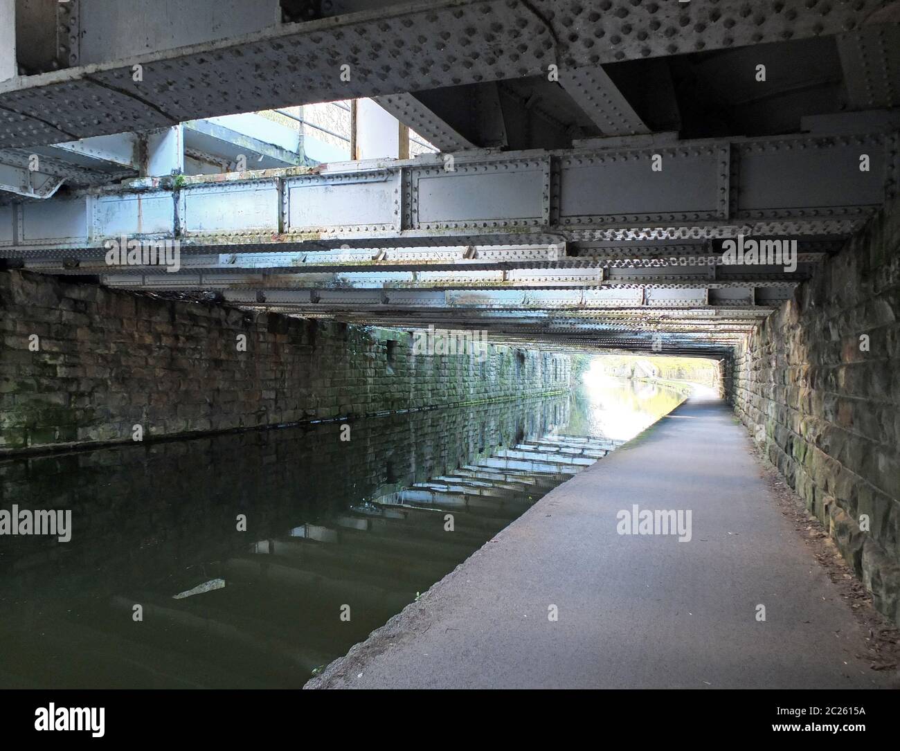 vue sous un vieux pont de poutres en acier bas traversant le canal leeds-liverpool près d'armley avec mur en pierre et un pied étroit Banque D'Images