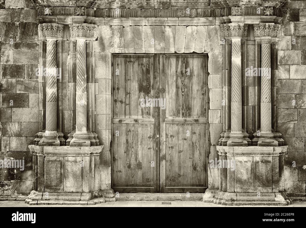 sépia monochrome anciennes portes doubles en bois dans un ancien bâtiment en pierre avec des colonnes ornées en ruines entourant l'entrée Banque D'Images