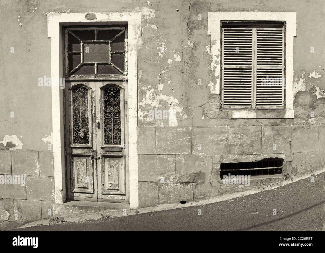 l'avant d'une ancienne maison abandonnée avec des fenêtres avec volets et porte en bois fermée avec des éclats de peinture sur une rue en pente Banque D'Images