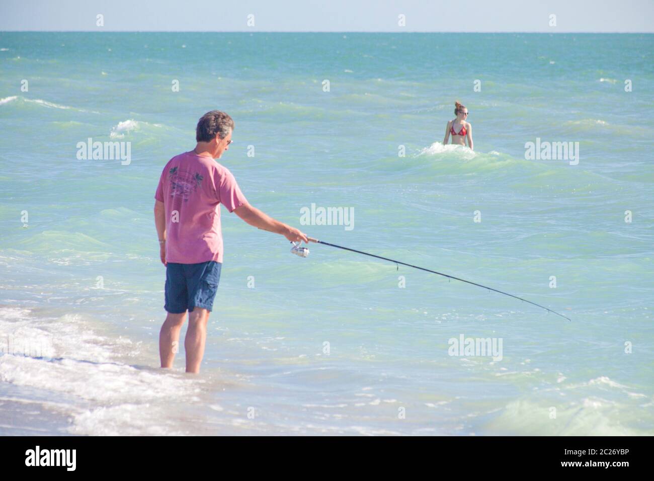 Homme avec la canne et la ligne de pêche en mer tandis que la femme bathes Banque D'Images