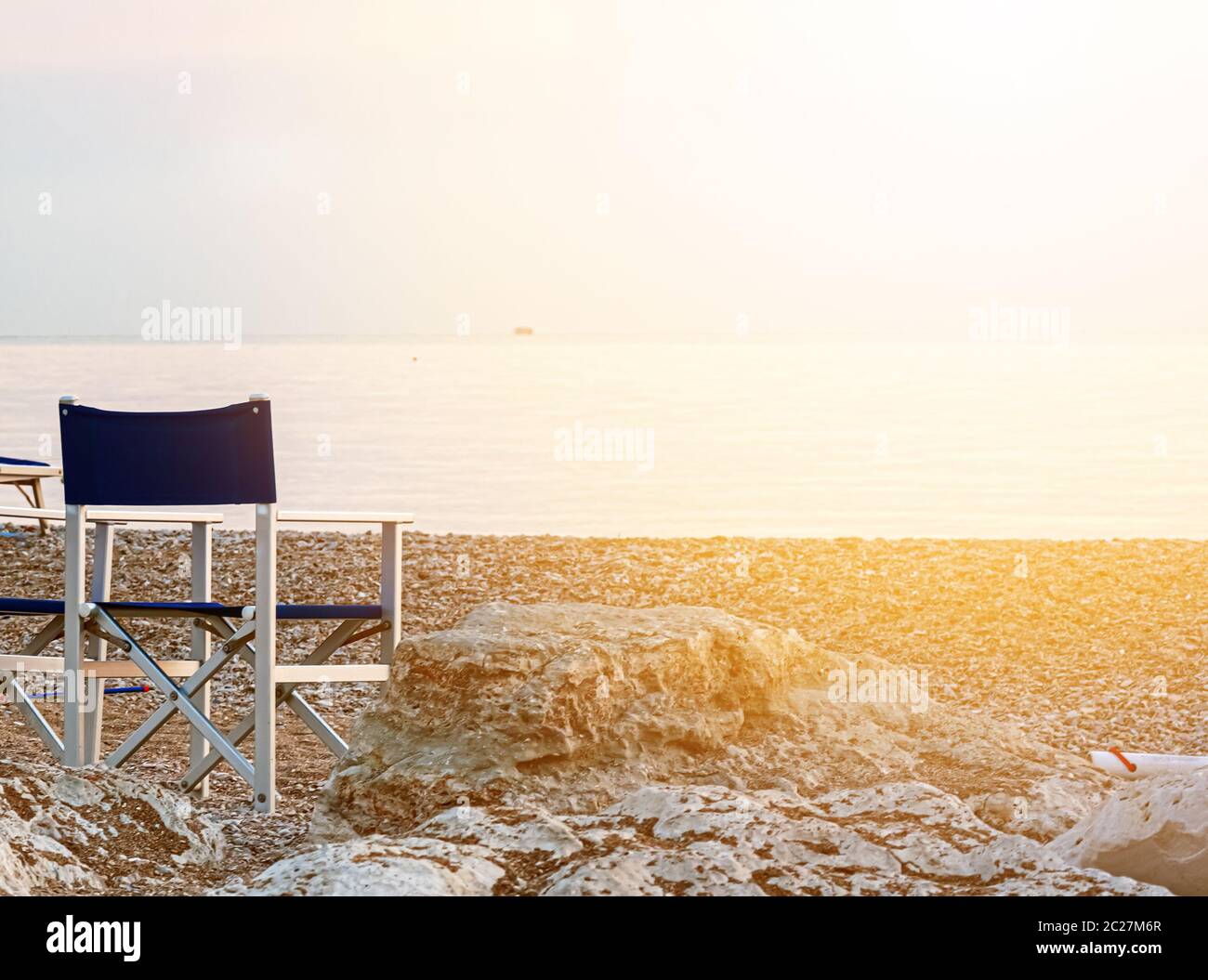 chaise d'extérieur pliante et vide sur une plage de galets éclairée par la lumière de l'aube au-dessus de la mer. Banque D'Images