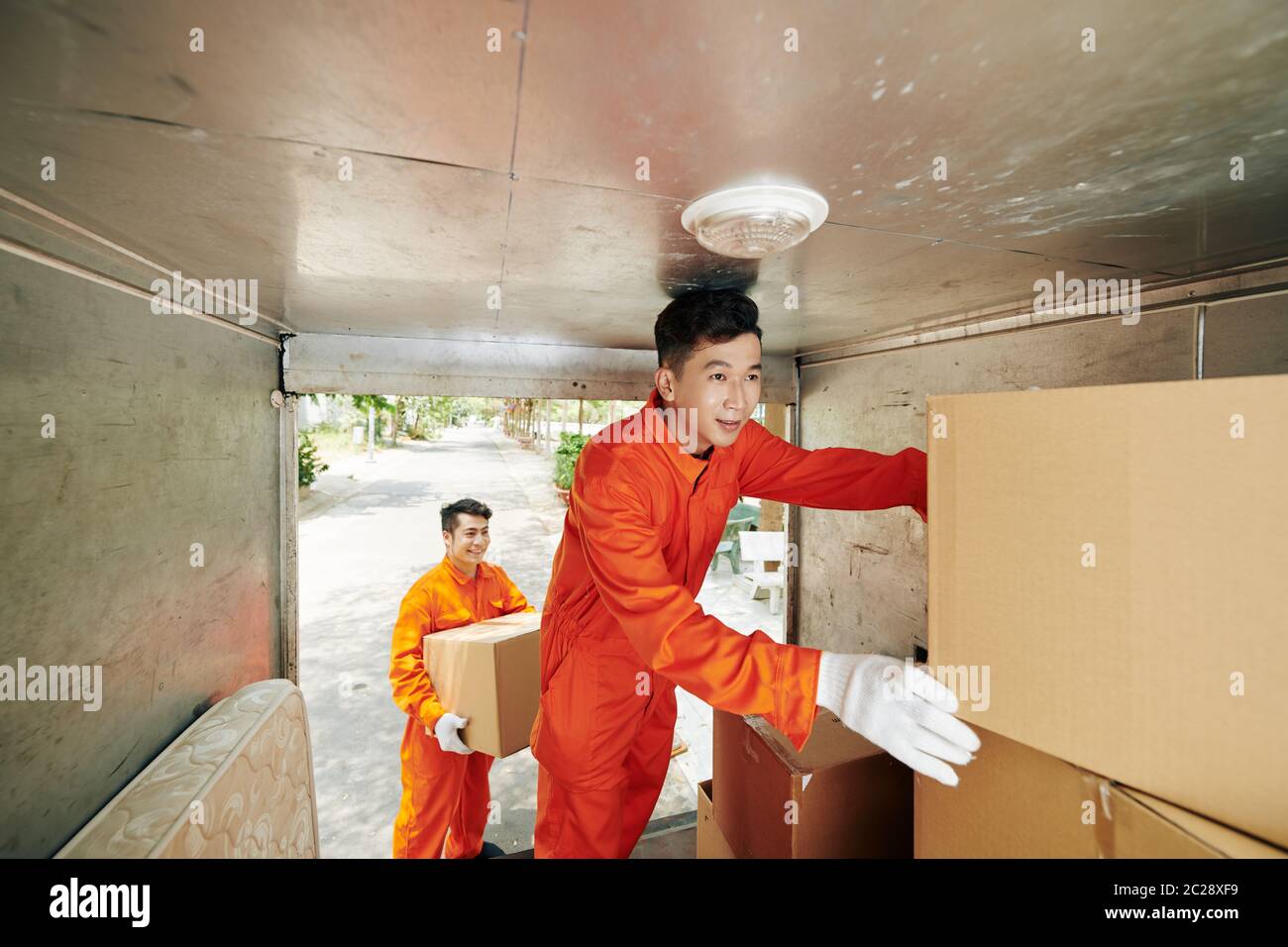 Deux jeunes hommes asiatiques adultes travaillant dans une maison moderne déplaçant des boîtes de levage de service dans une camionnette, plan horizontal Banque D'Images