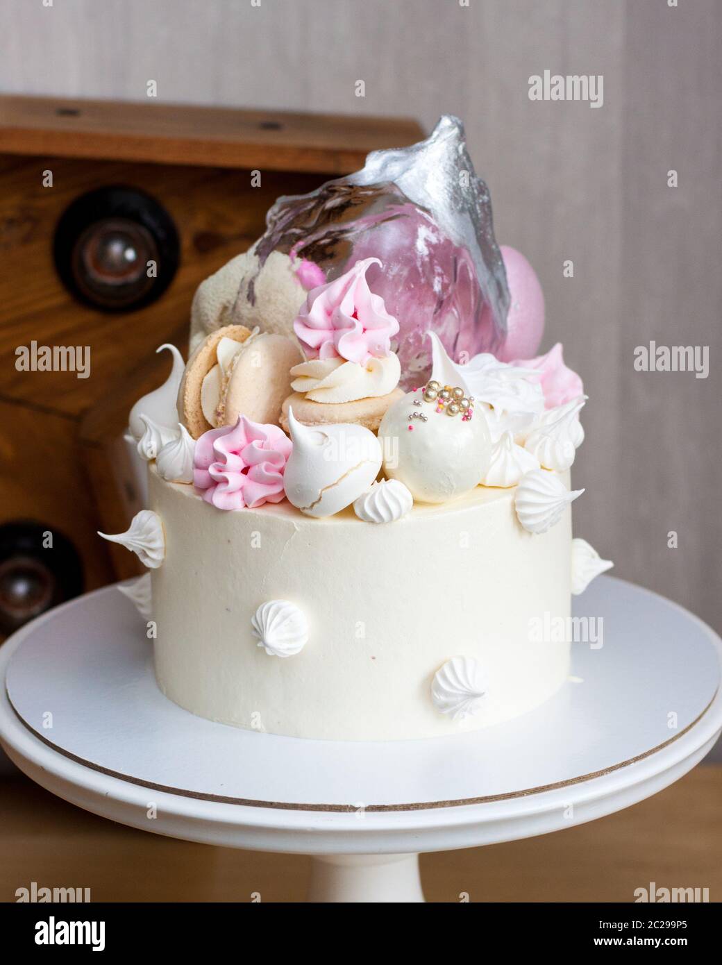 Gâteau blanc élégant avec de l'isomalt, du chocolat, des macarons, des meringues, des éléments roses et argentés. Banque D'Images