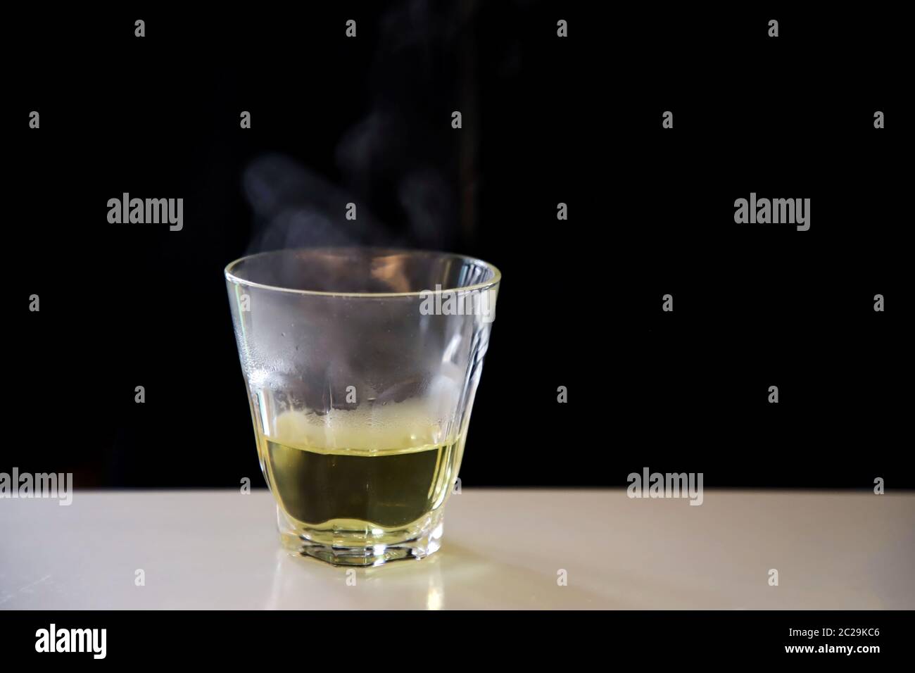 Thé chinois chaude fumée basé sur un verre transparent placé sur un tableau blanc sur fond noir. Banque D'Images