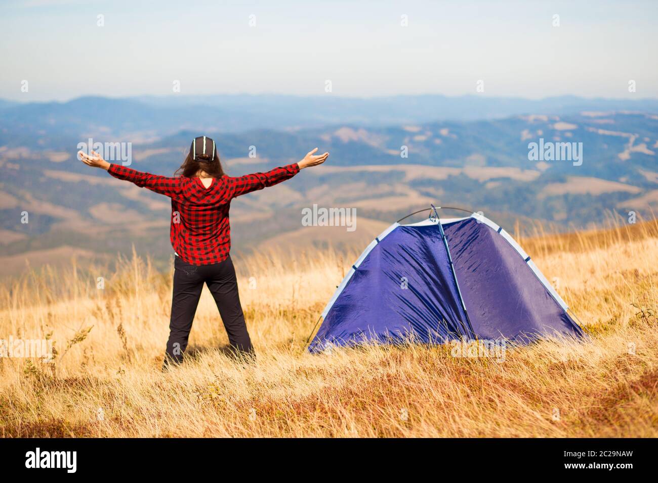 Vue arrière de la femme randonnée sentier de montagne, debout près de la tente avec les mains vers le haut, appréciant matin d'été dans les montagnes Carpathian. Camping aventure vacatio Banque D'Images