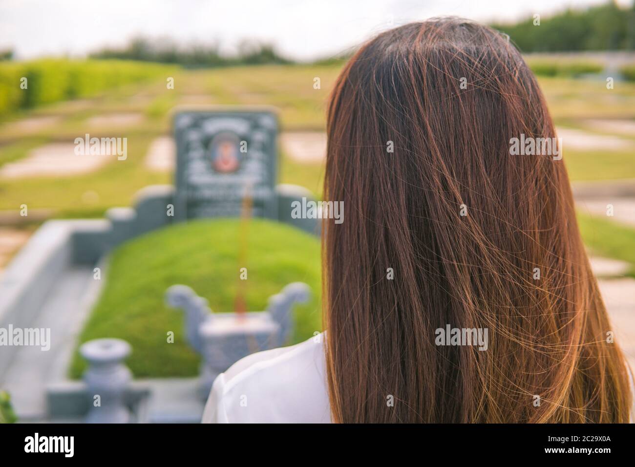 Une femme non identifiée éclaire l'encens, prosterant devant une tombe non identifiée dans le cimetière, jardin du sala, long Thanh, Vietnam. Concept de Banque D'Images