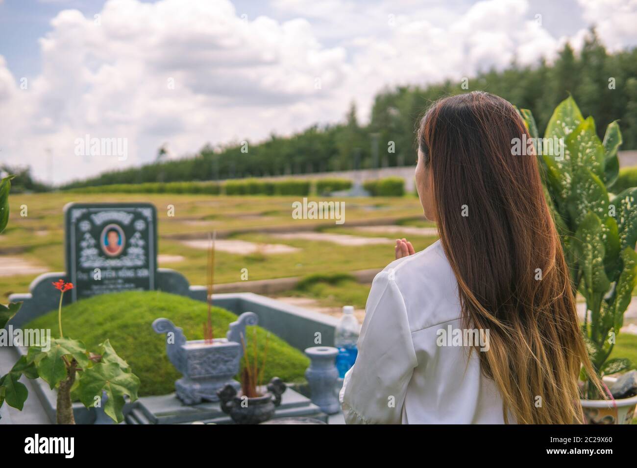 Une femme non identifiée éclaire l'encens, prosterant devant une tombe non identifiée dans le cimetière, jardin du sala, long Thanh, Vietnam. Concept de Banque D'Images