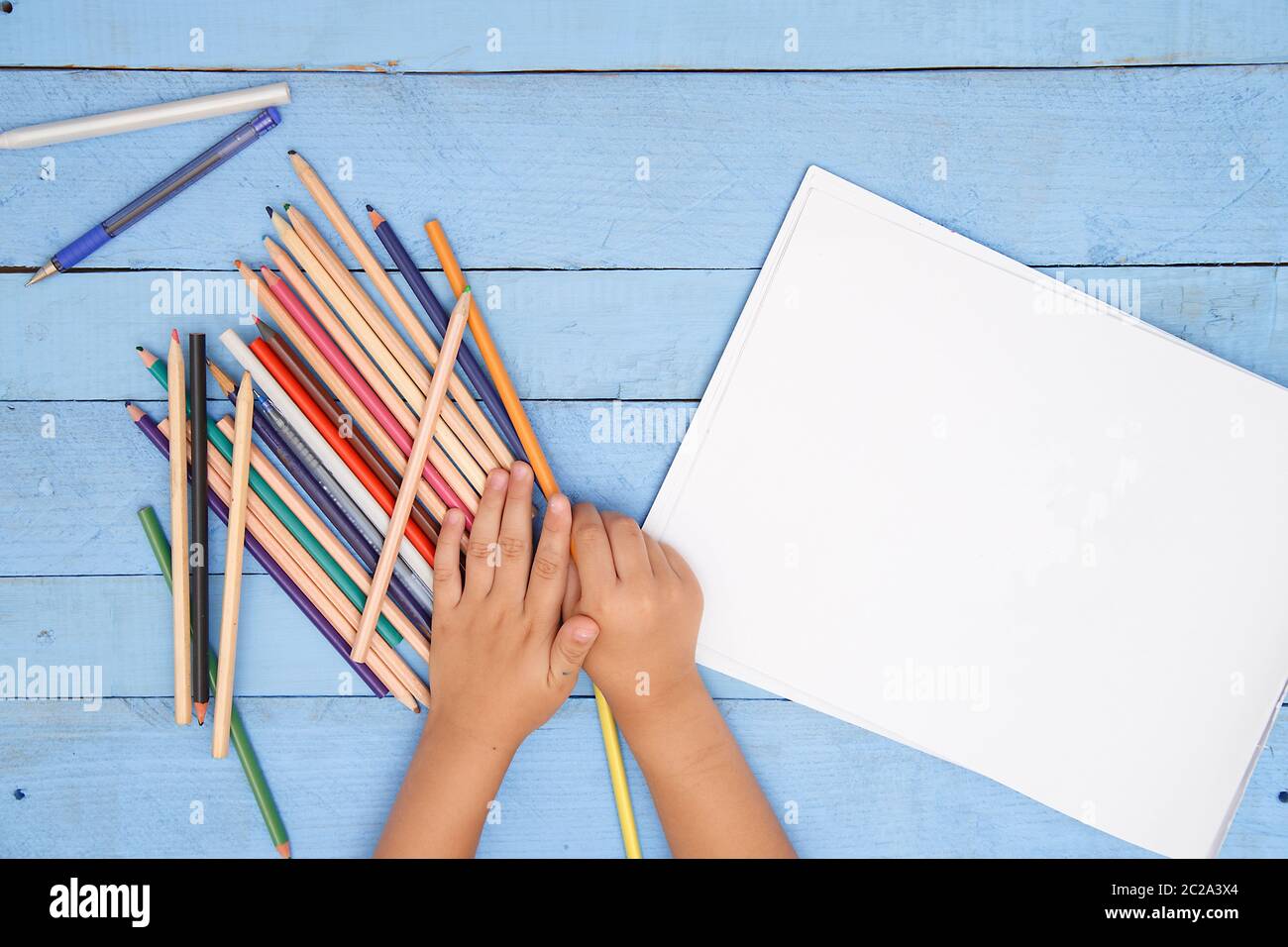 Les mains des enfants dessiner avec des crayons dans l'album sur la table bleu Banque D'Images