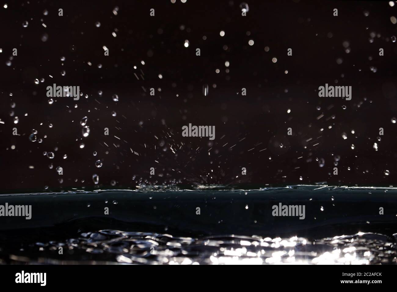 Beaucoup de petits gouttes de pluie gécoutent au soleil. La pluie tombe sur le sol Banque D'Images